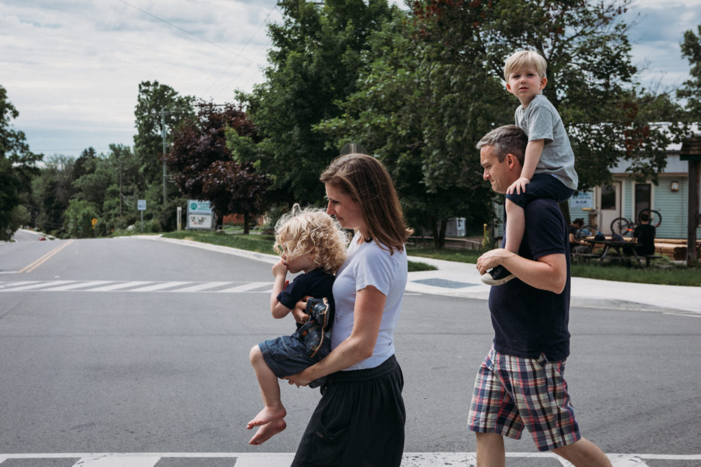 colour photo of family of four crossing the street with both kids in their parents' arms