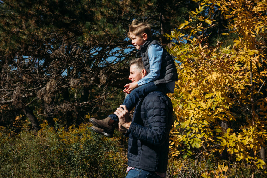 photo of child sitting on dad's shoulders with bright yellow fall leaves behind them